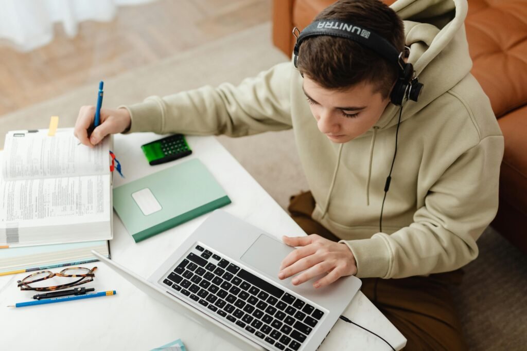 Teen studying at home with laptop, books, and headphones, focused on learning.